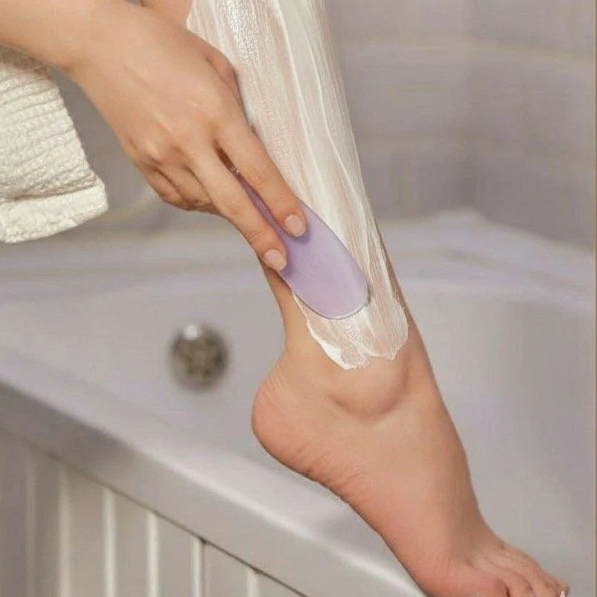 Женщина наносит крем для замедления роста волос на ногу